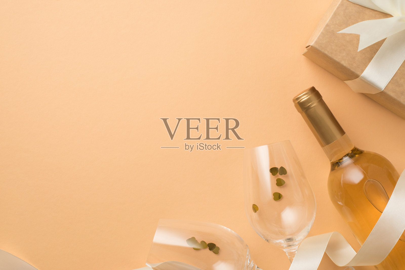 俯视图照片的情人节装饰葡萄酒酒瓶,葡萄酒杯与心形的彩纸丝绸丝带和牛皮纸礼盒白色蝴蝶结在孤立的粉彩米色背景与空空间照片摄影图片