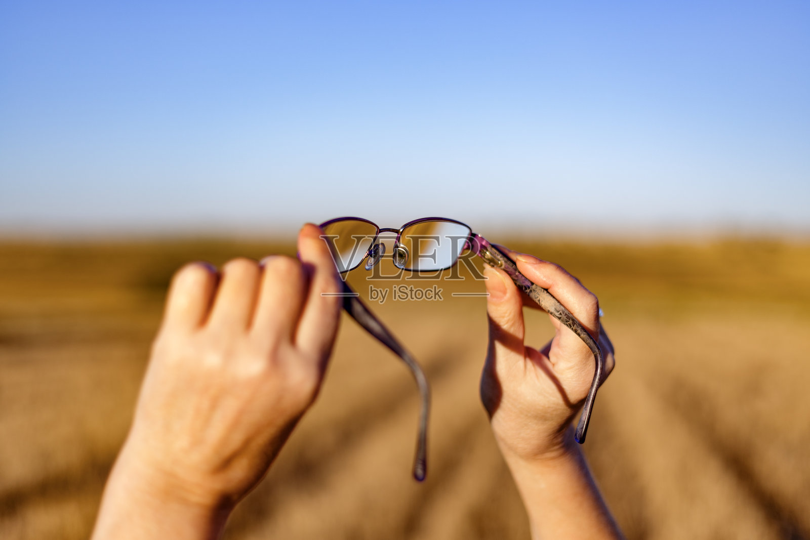 在日落时,手握眼镜在散焦的阳光场背景上。马德里,西班牙照片摄影图片