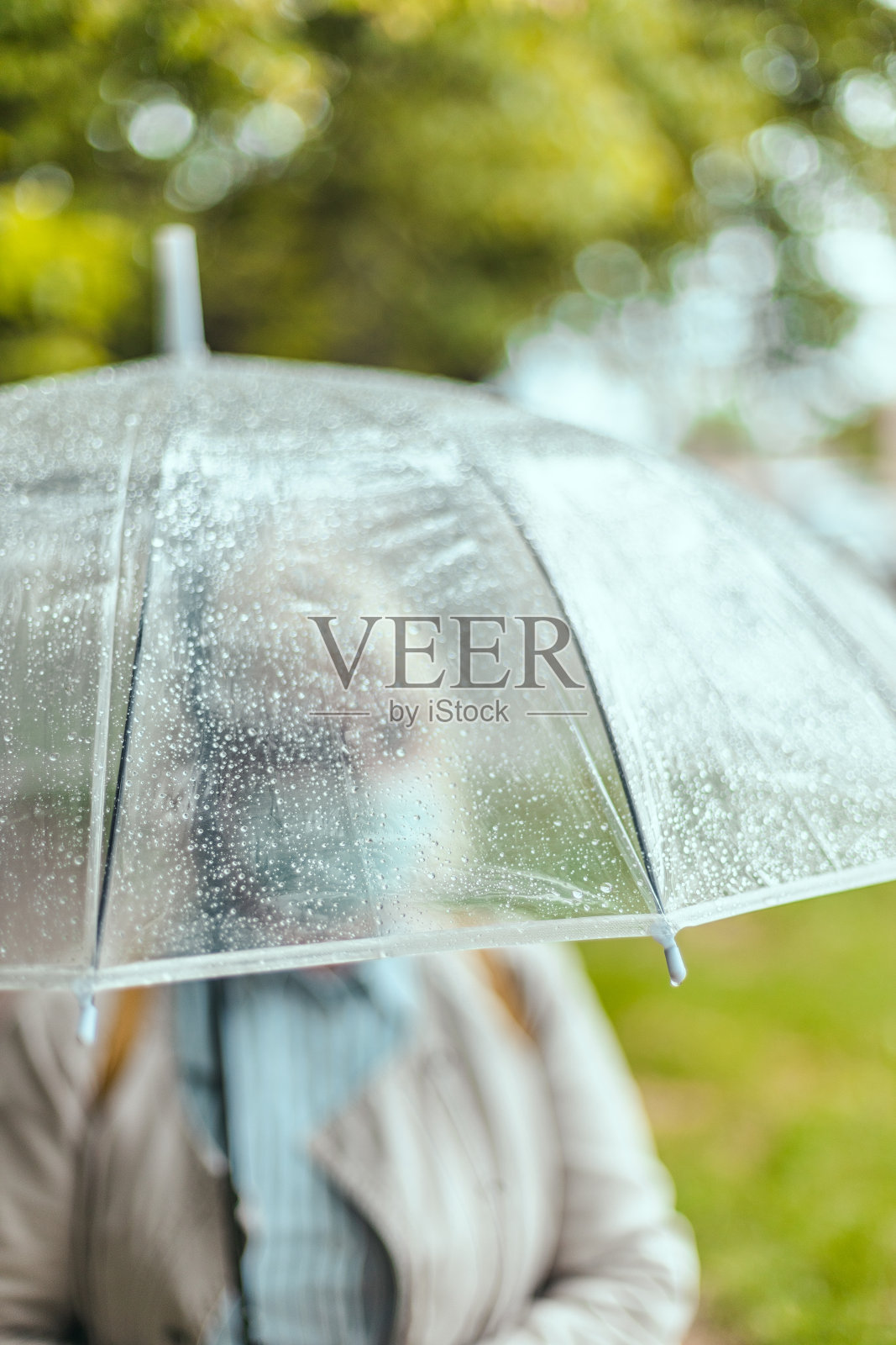 在城市公园里,一位穿着鲜艳衣服的老妇人撑着一把透明的雨伞,伸直的手在恶劣的天气里抓着水滴照片摄影图片