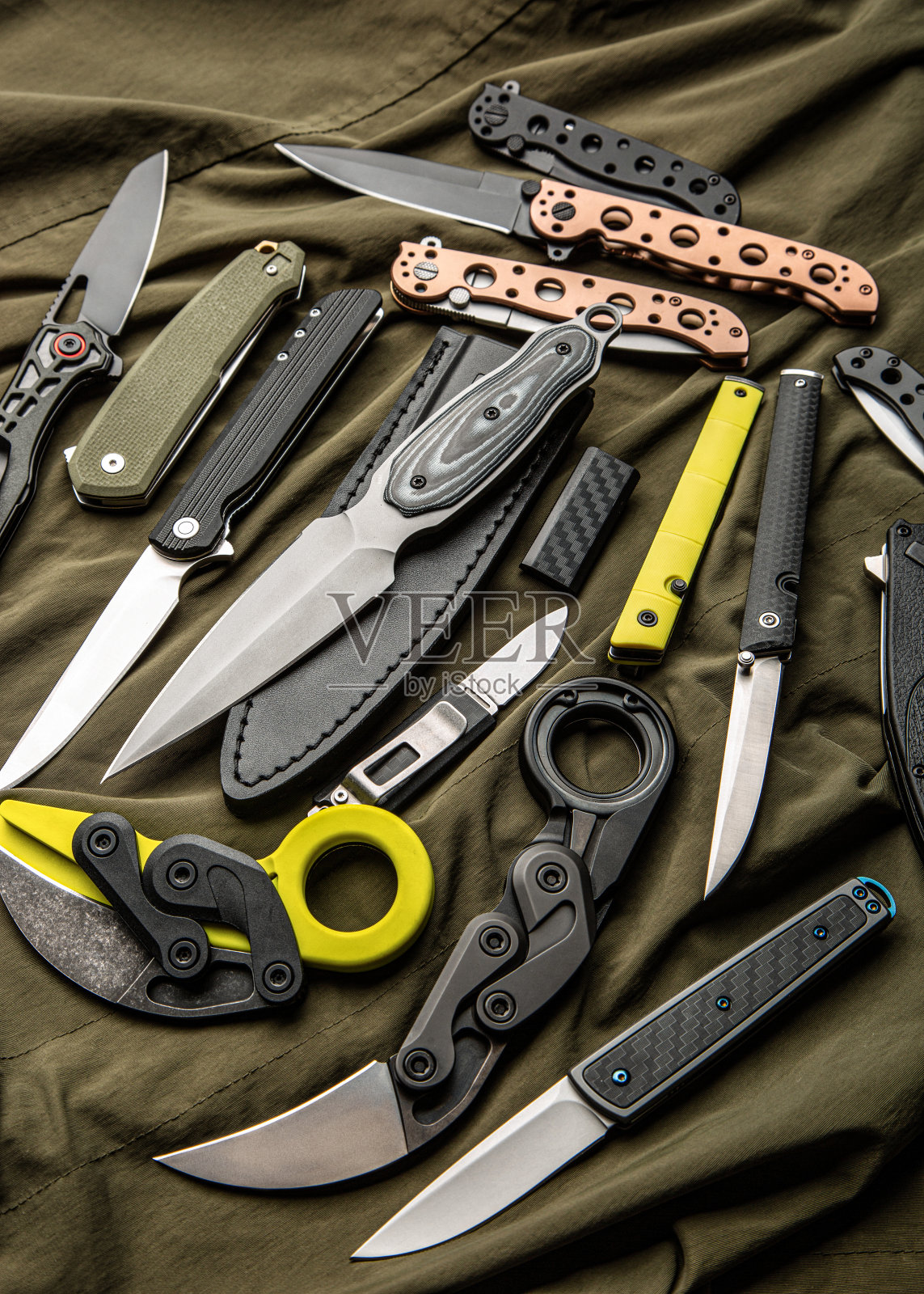 各种折叠刀和折刀躺在卡其织物上。一种多功能的口袋工具和自卫工具。照片摄影图片