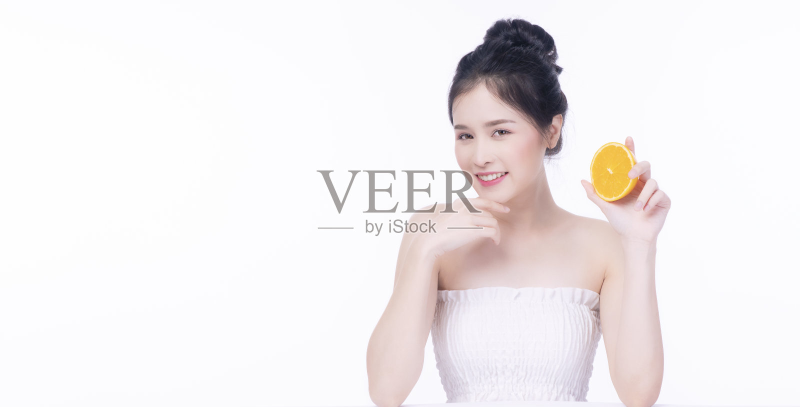 快乐的亚洲妇女持有新鲜的橙子片维生素c为好皮肤看着相机在孤立的白色背景。保健肤色活力或饮食生活方式的理念。照片摄影图片