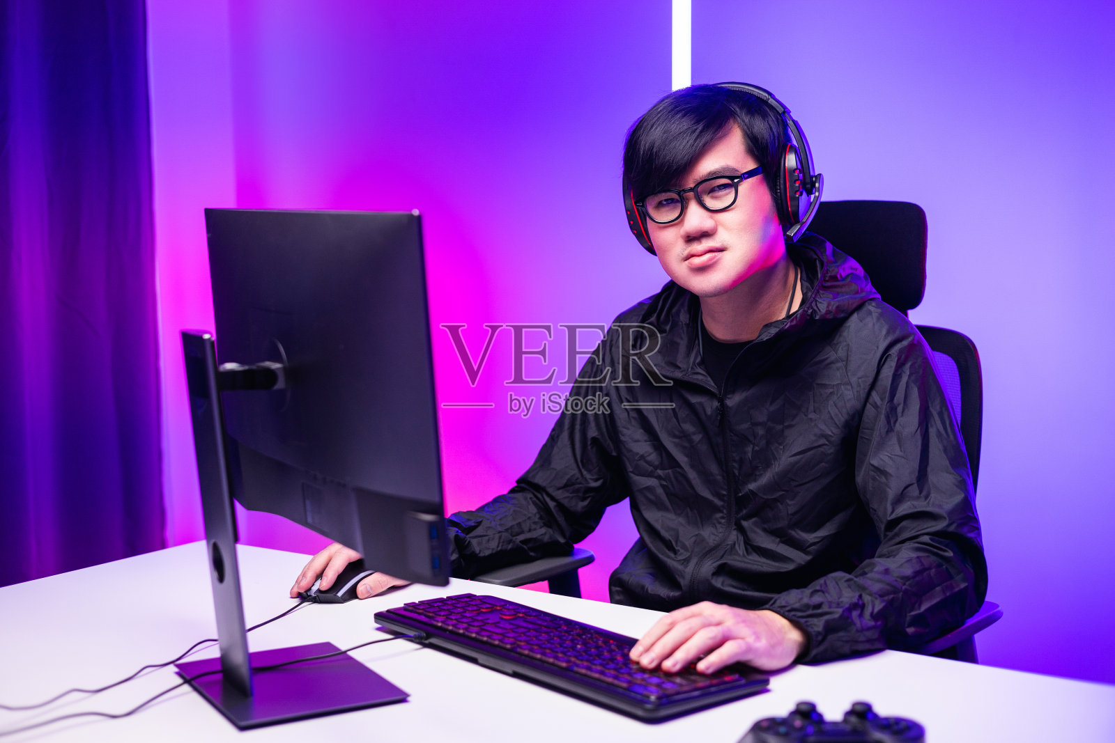 亚洲玩家带着耳机在客厅里玩电脑游戏。年轻的职业玩家流媒体社交玩游戏非常有趣照片摄影图片