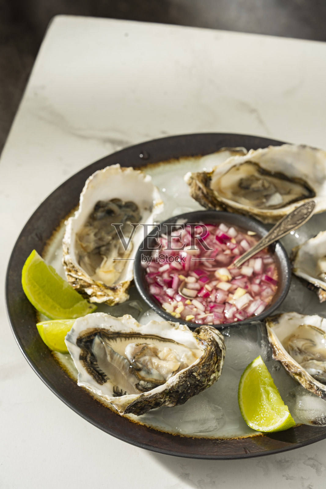 灰色圆形盘子里盛着新鲜的牡蛎和酸橙、洋葱。牡蛎的季节。宏海鲜菜肴。照片摄影图片