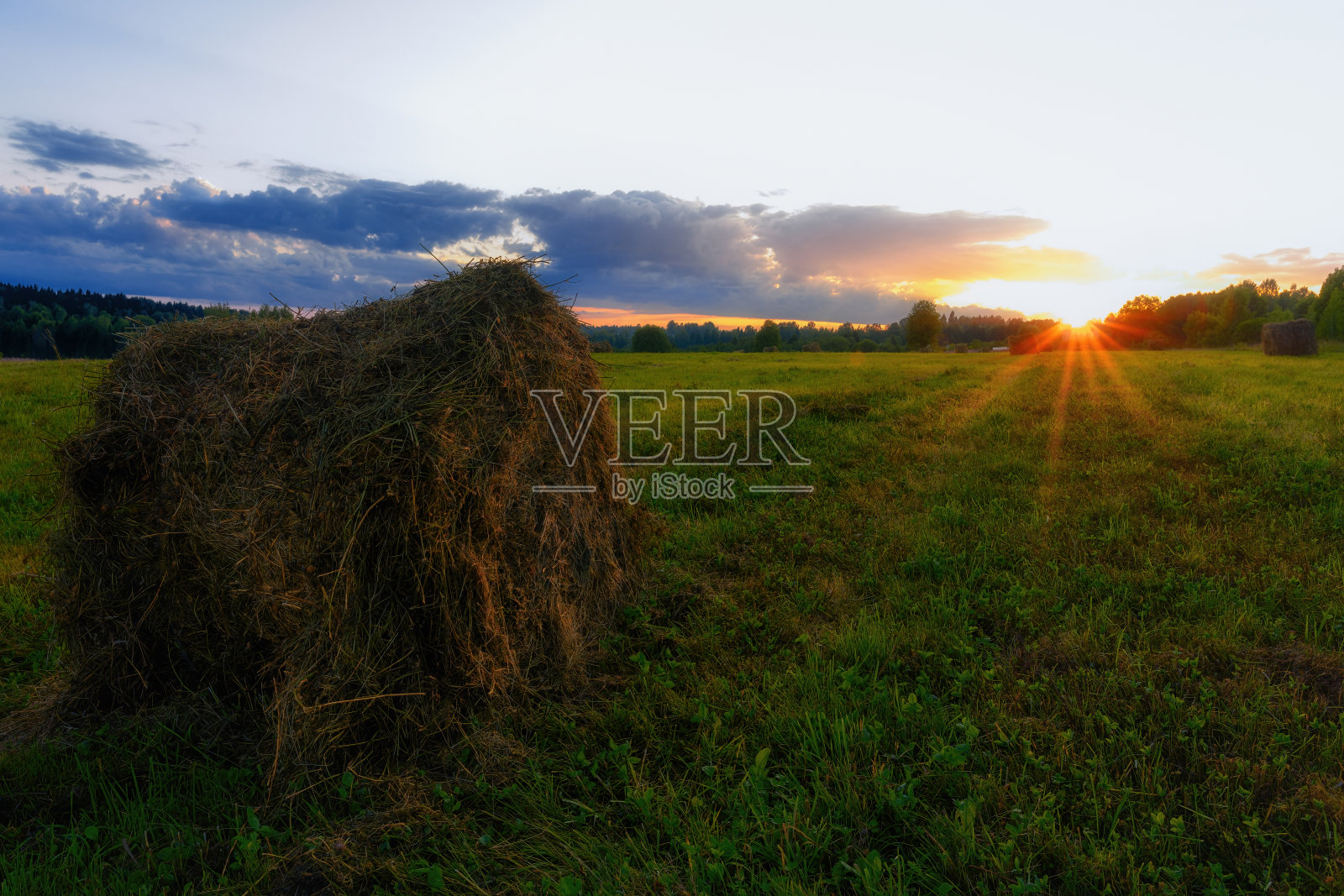 最后一缕阳光照在草堆上。辛苦的收割干草的一天结束了。照片摄影图片