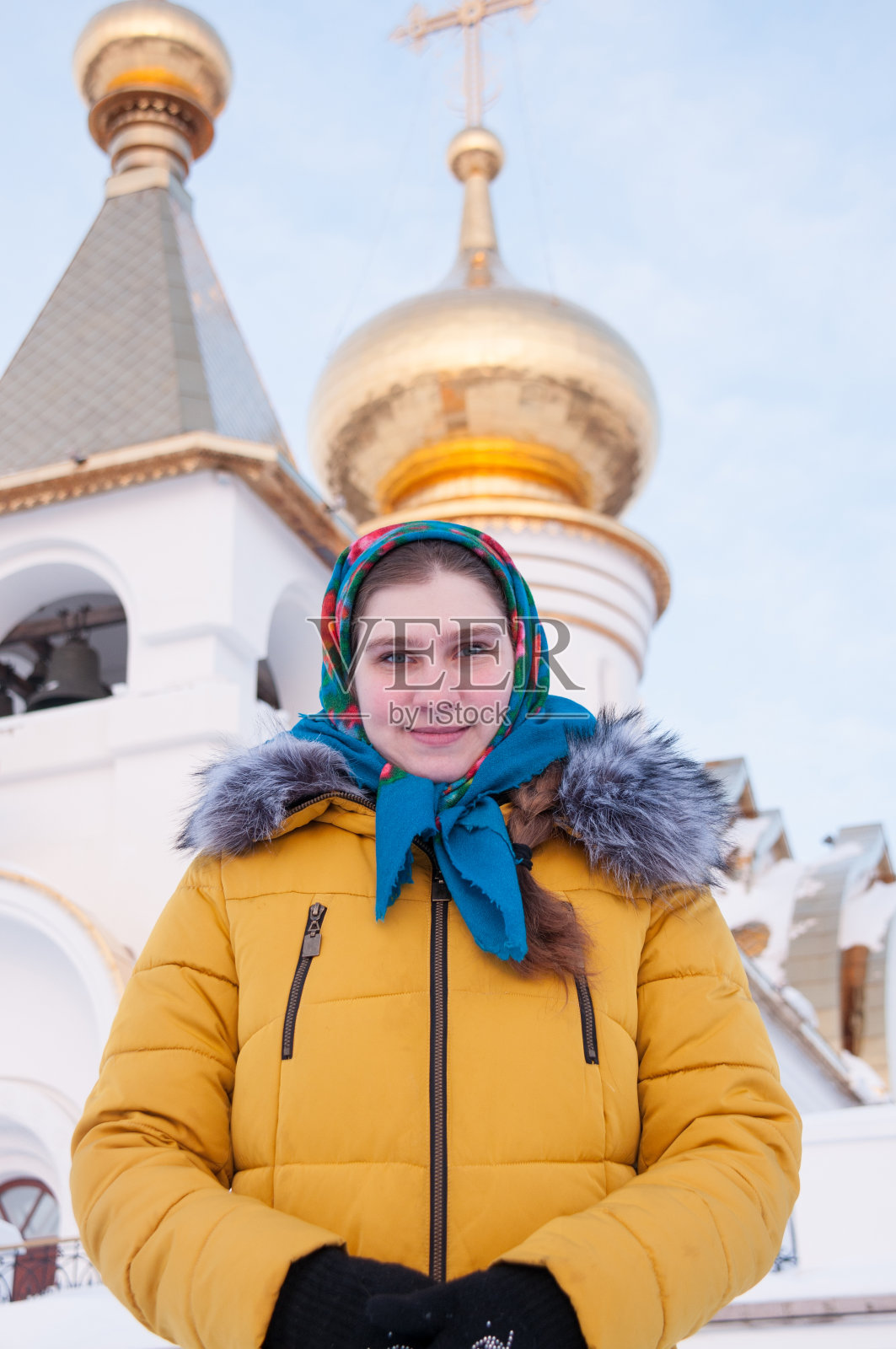 冬天,一个女孩披着俄罗斯人的披肩,穿着黄色羽绒服,背景是一座东正教教堂照片摄影图片