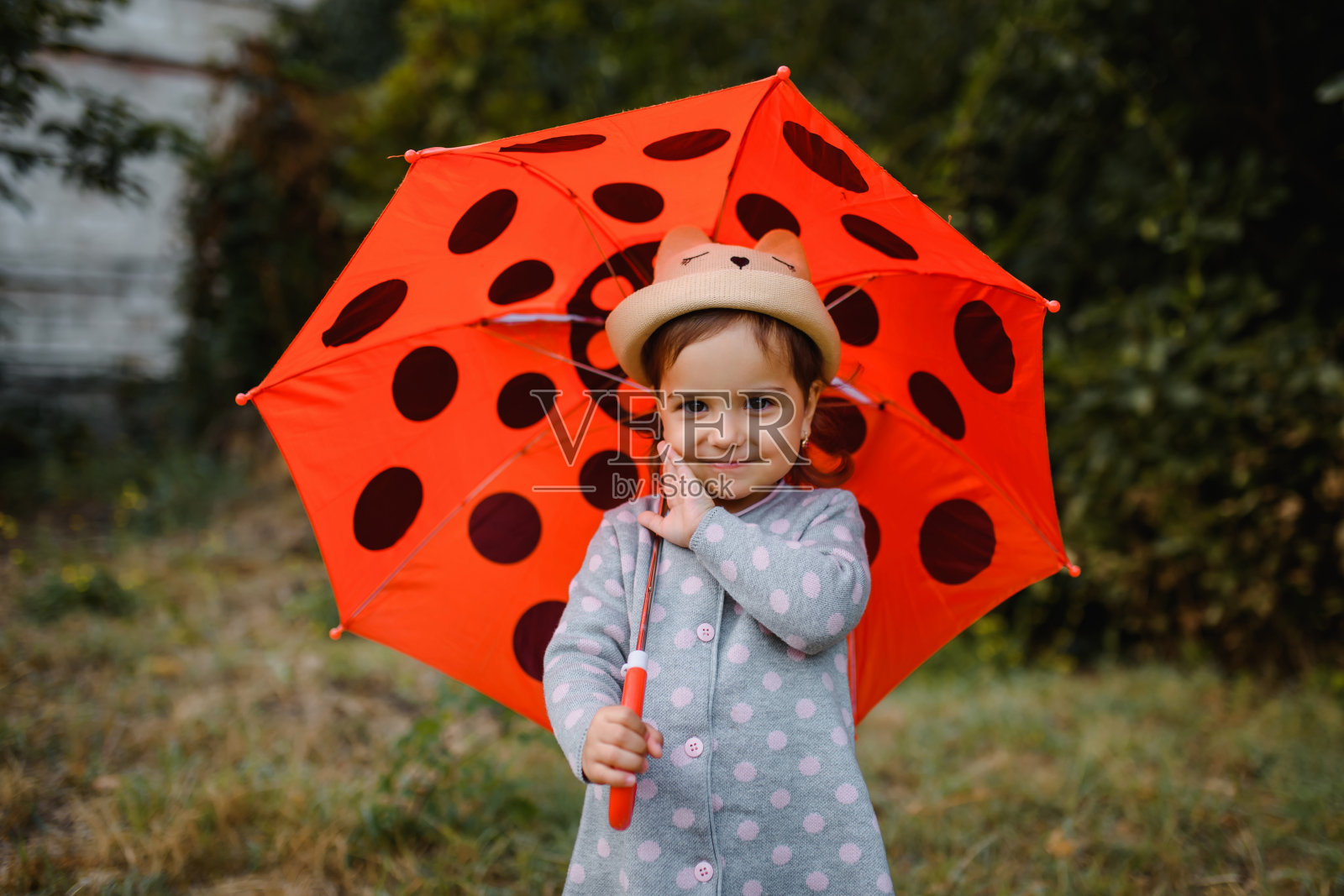 一个快乐微笑的2岁小女孩的肖像,在户外拿着她的红色圆点伞。照片摄影图片