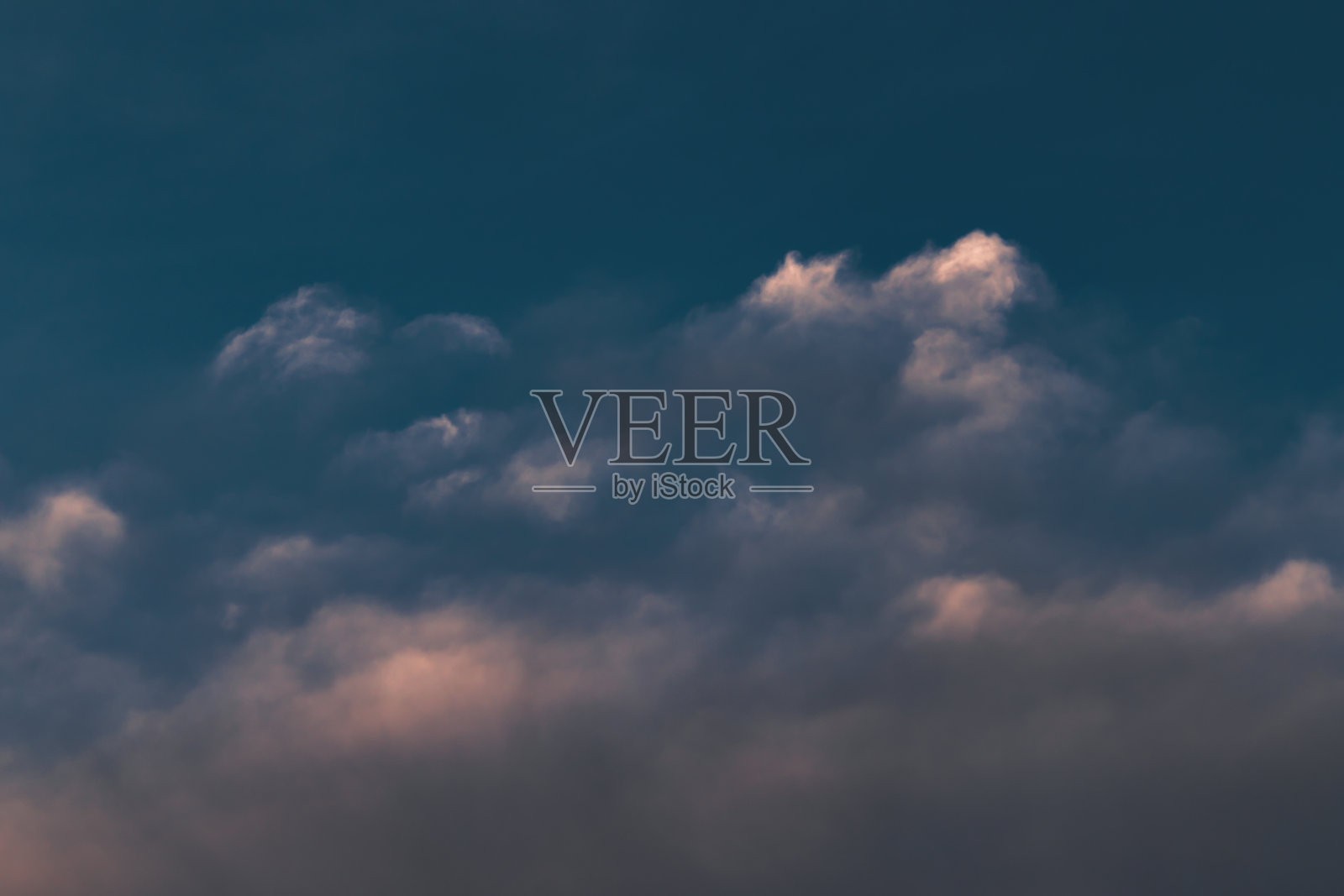 一大片云浸在阴影里,阳光只照在它顶上的几簇云上。照片摄影图片