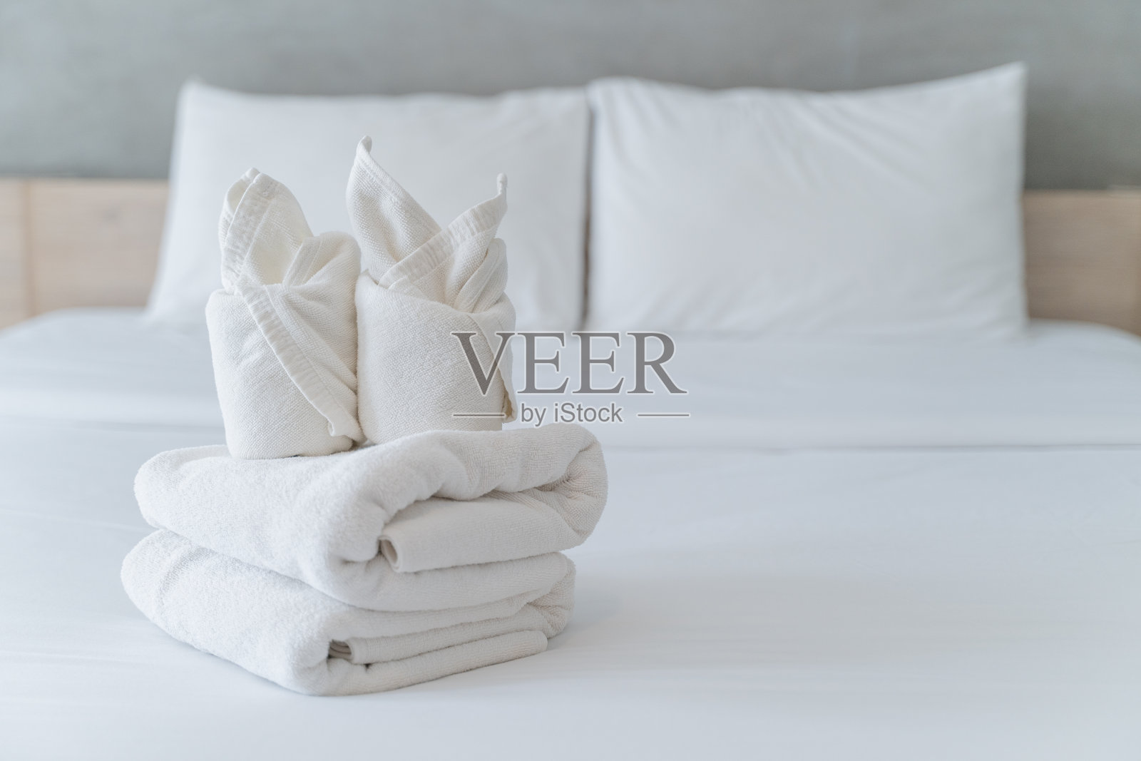 在酒店干净舒适的卧室里,折叠柔软的白色毛巾放在白色的床上迎接客人照片摄影图片