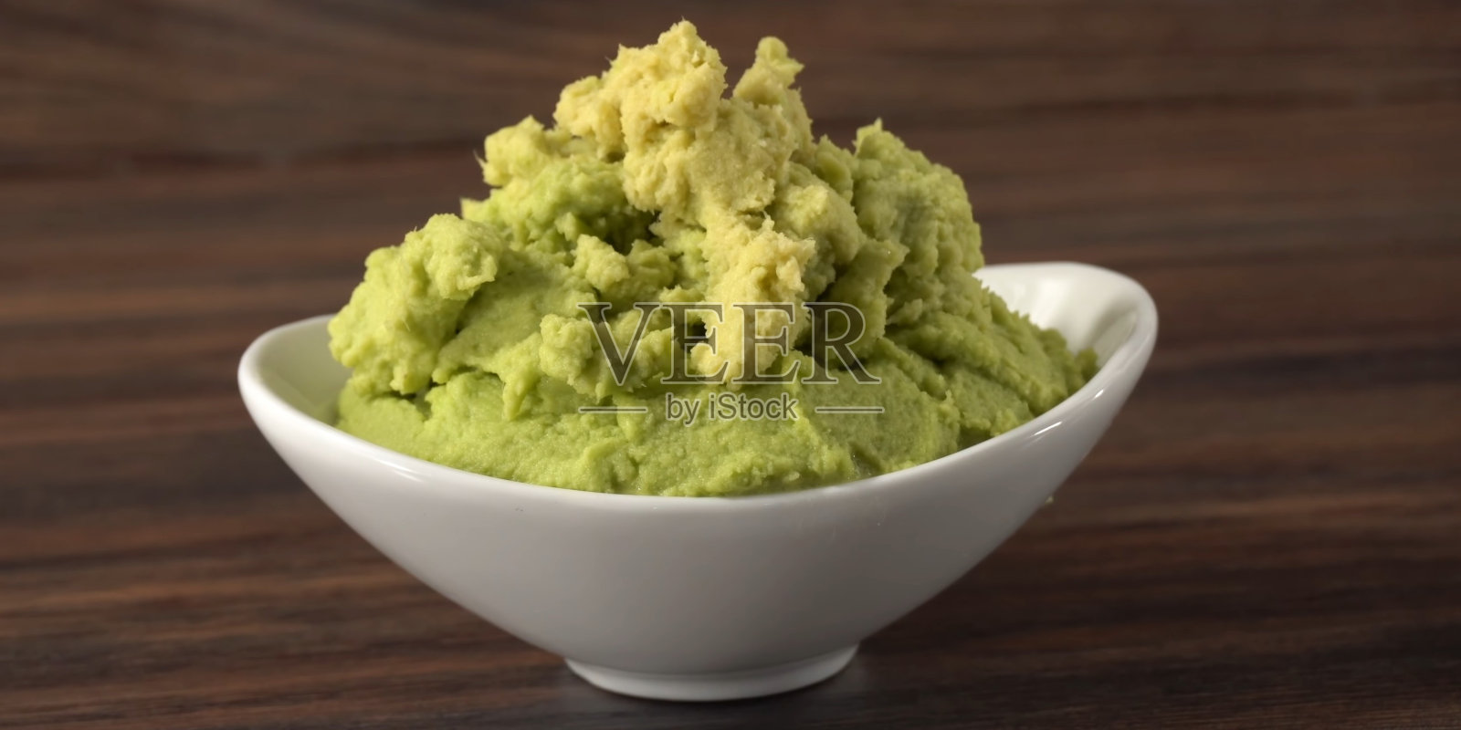 芥末蘸酱。盛在碗里的绿芥末酱或酱汁。木质背景的日本芥末酱。照片摄影图片