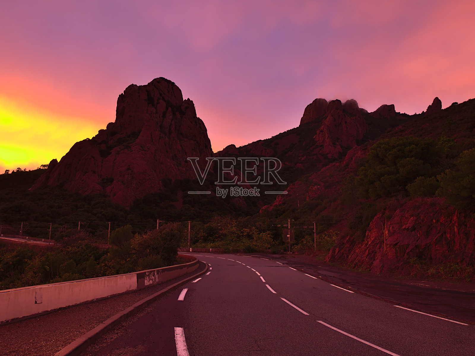 秋天,在法国里维埃拉的圣拉斐尔附近,日落后,可以看到地中海海岸的Roux海角崎岖的岩石和D559蜿蜒的公路,以及色彩鲜艳的天空。照片摄影图片