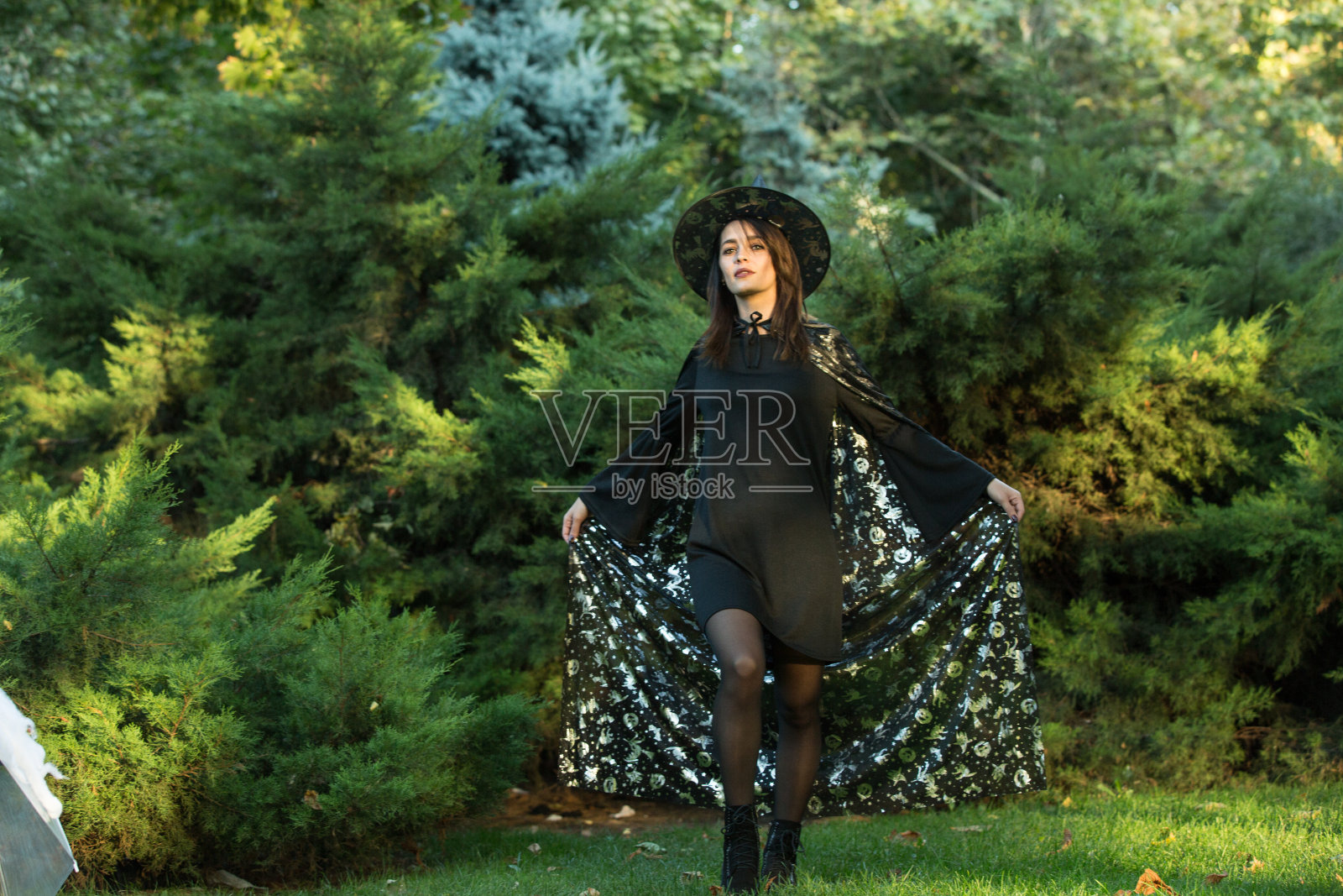 在绿色森林的背景上,一个有吸引力的年轻女人穿着黑色裙子和披肩的肖像。照片摄影图片