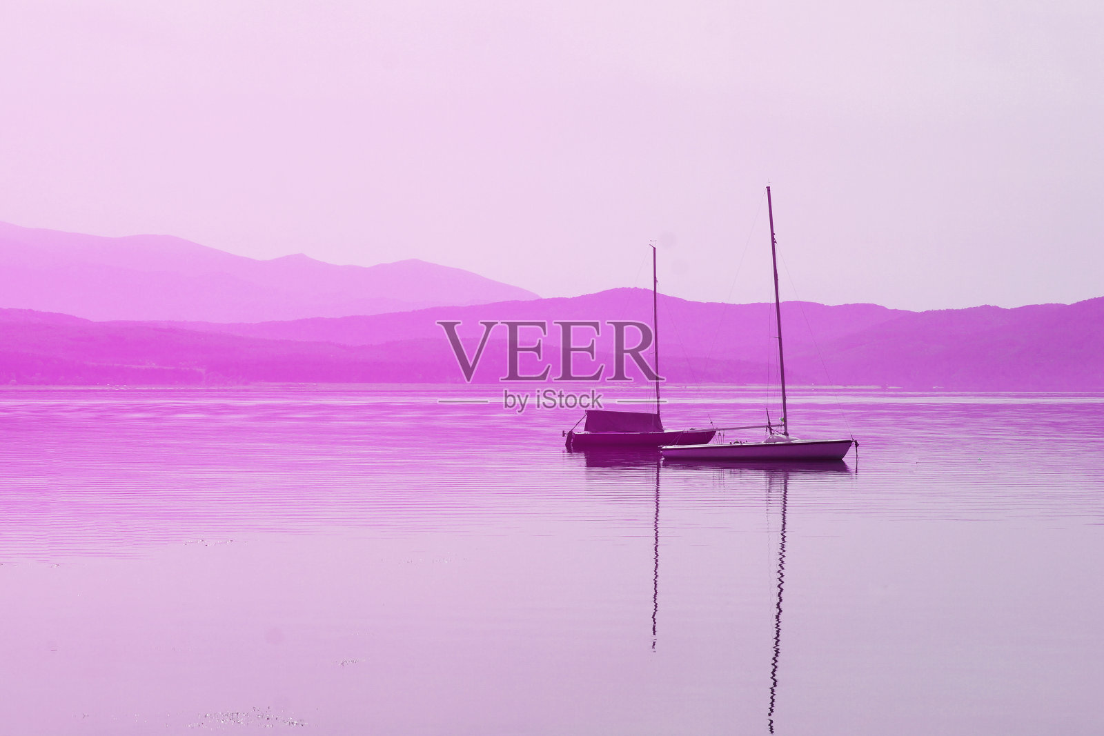 在粉红色的山脉背景下,水面上的船和桅杆照片摄影图片