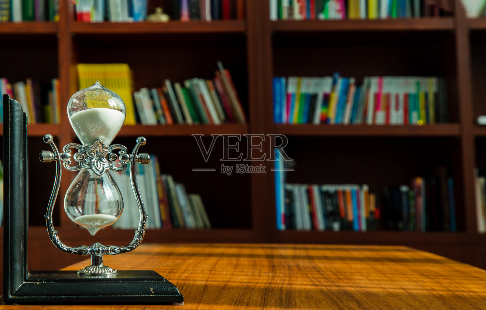 桌子上的沙漏,背景是图书馆的书架。照片摄影图片