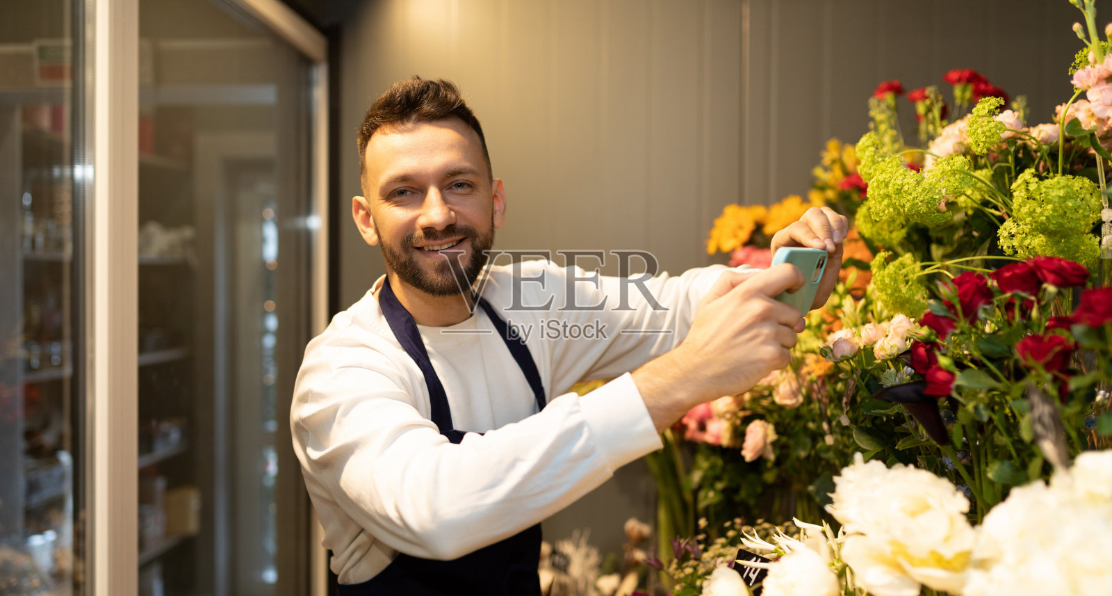 一位成功的企业家在自己的商店里拿着鲜花站在冰箱里,微笑着看着镜头照片摄影图片