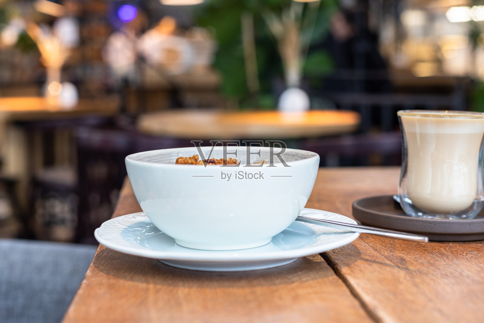 木桌上放着一碗燕麦片和一杯卡布奇诺,模糊的咖啡背景。健康美味的早餐配燕麦粥。照片摄影图片