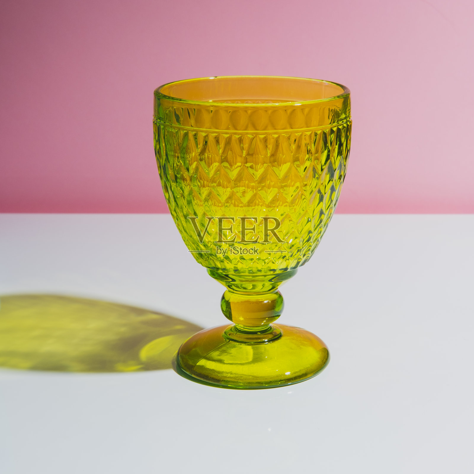 一个时尚的绿色多面玻璃与阴影在白色的桌子与粉红色的背景。最小的艺术。照片摄影图片