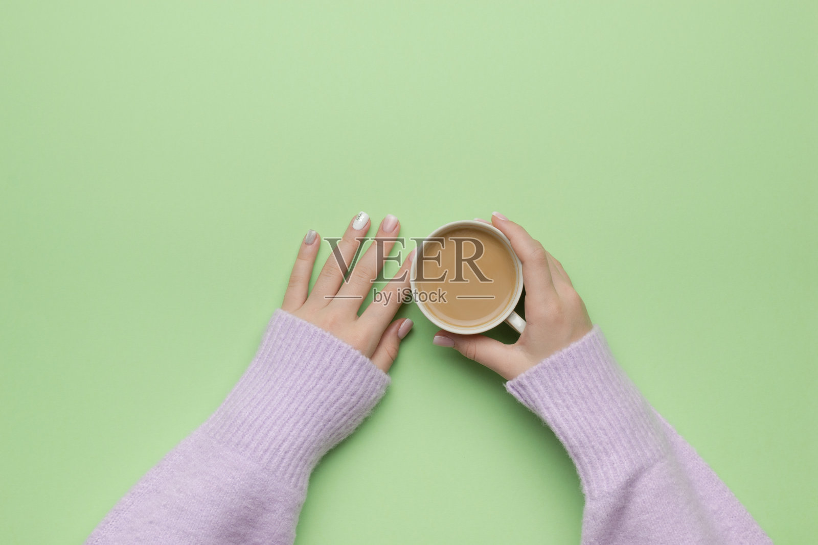 女性手穿紫色毛衣,绿色背景上放着一杯咖啡。平的。照片摄影图片