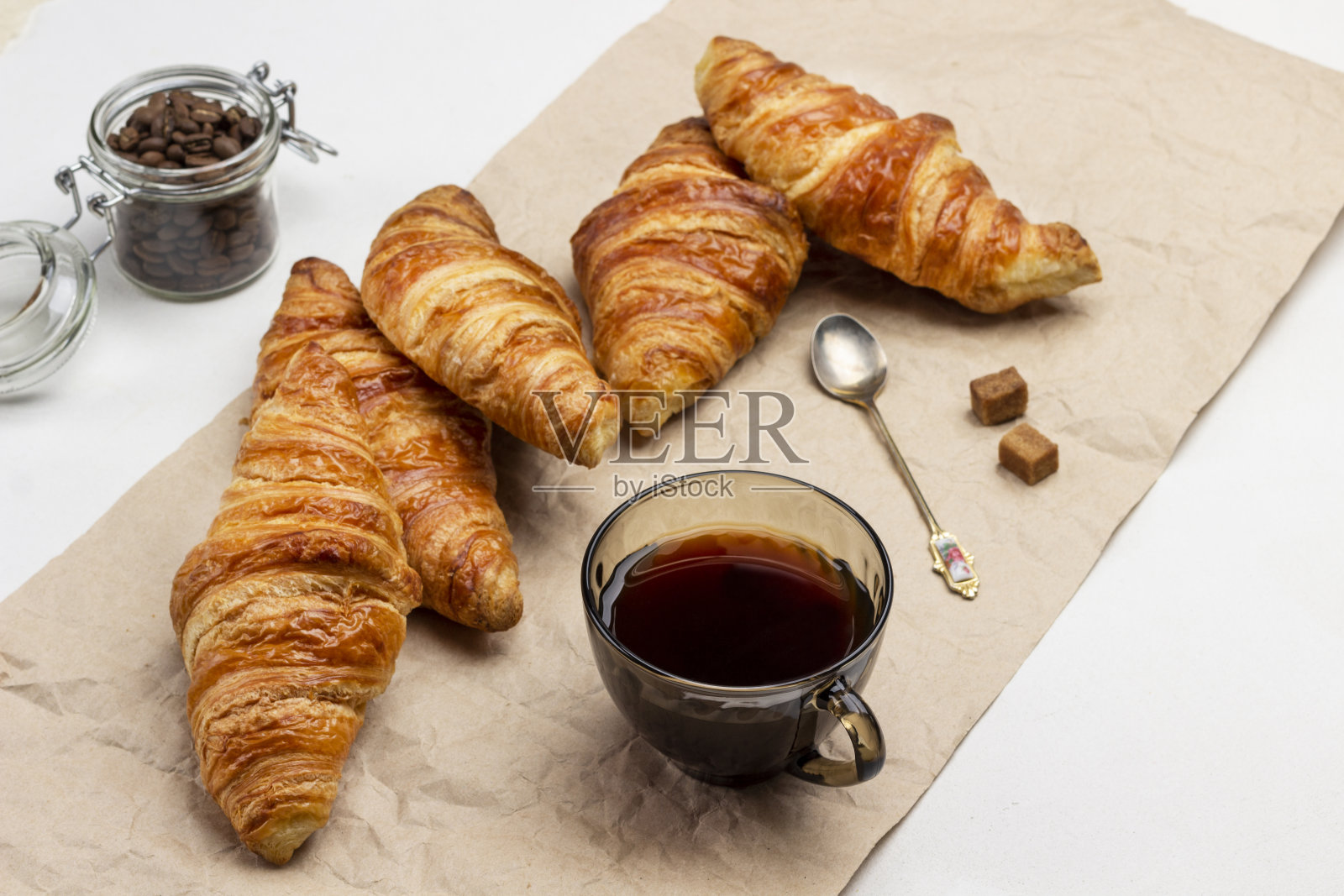 牛角面包和咖啡在纸上。在罐子里放上咖啡粒。照片摄影图片