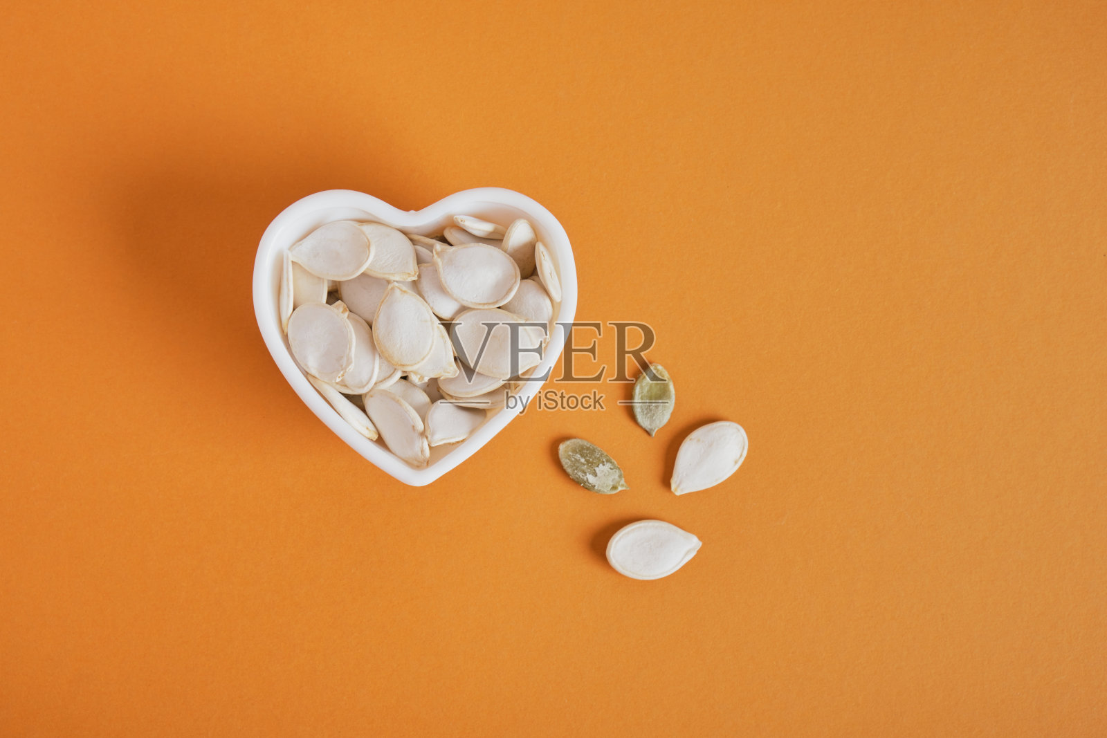 心形碗里的南瓜籽在棕色的背景上照片摄影图片