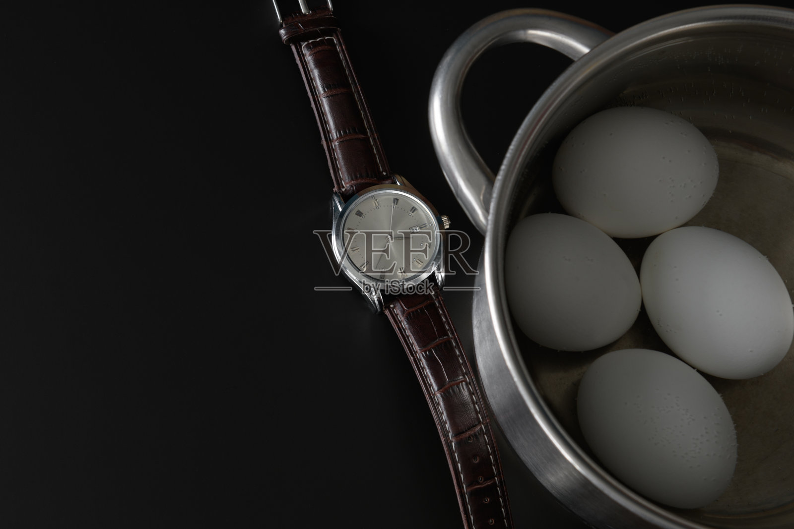 手表和煮鸡蛋在炖锅。在黑色的背景上照片摄影图片