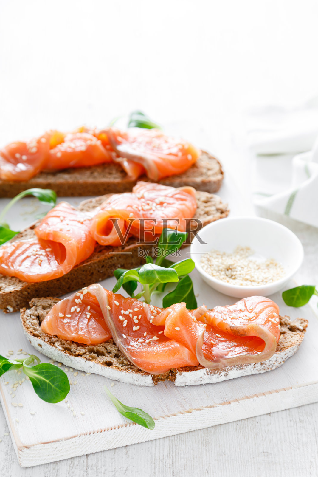 白色质朴的木桌上,全麦黑麦面包和腌鲑鱼三明治开放。健康的食物照片摄影图片