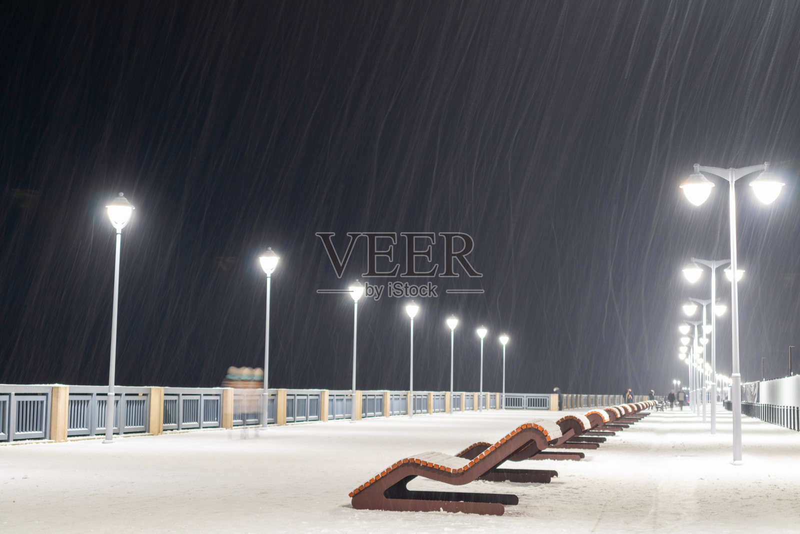 冬天的傍晚,在这个海滨小镇的木板路上,空荡荡的躺椅躺在雪下照片摄影图片