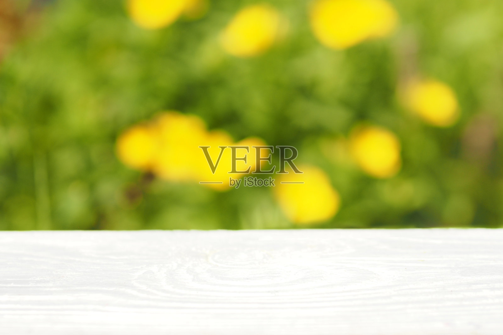 轻木桌面在背景上模糊的绿色的草和黄色的花。没有焦点。照片摄影图片