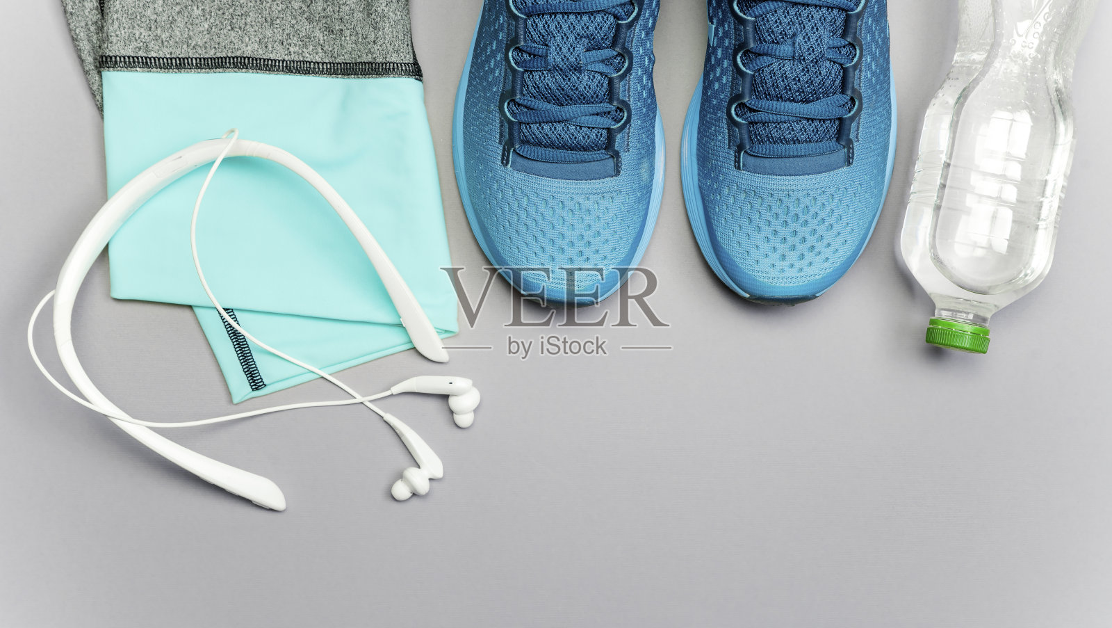 女子运动短裤,运动鞋,耳机和一个水瓶在灰光背景照片摄影图片