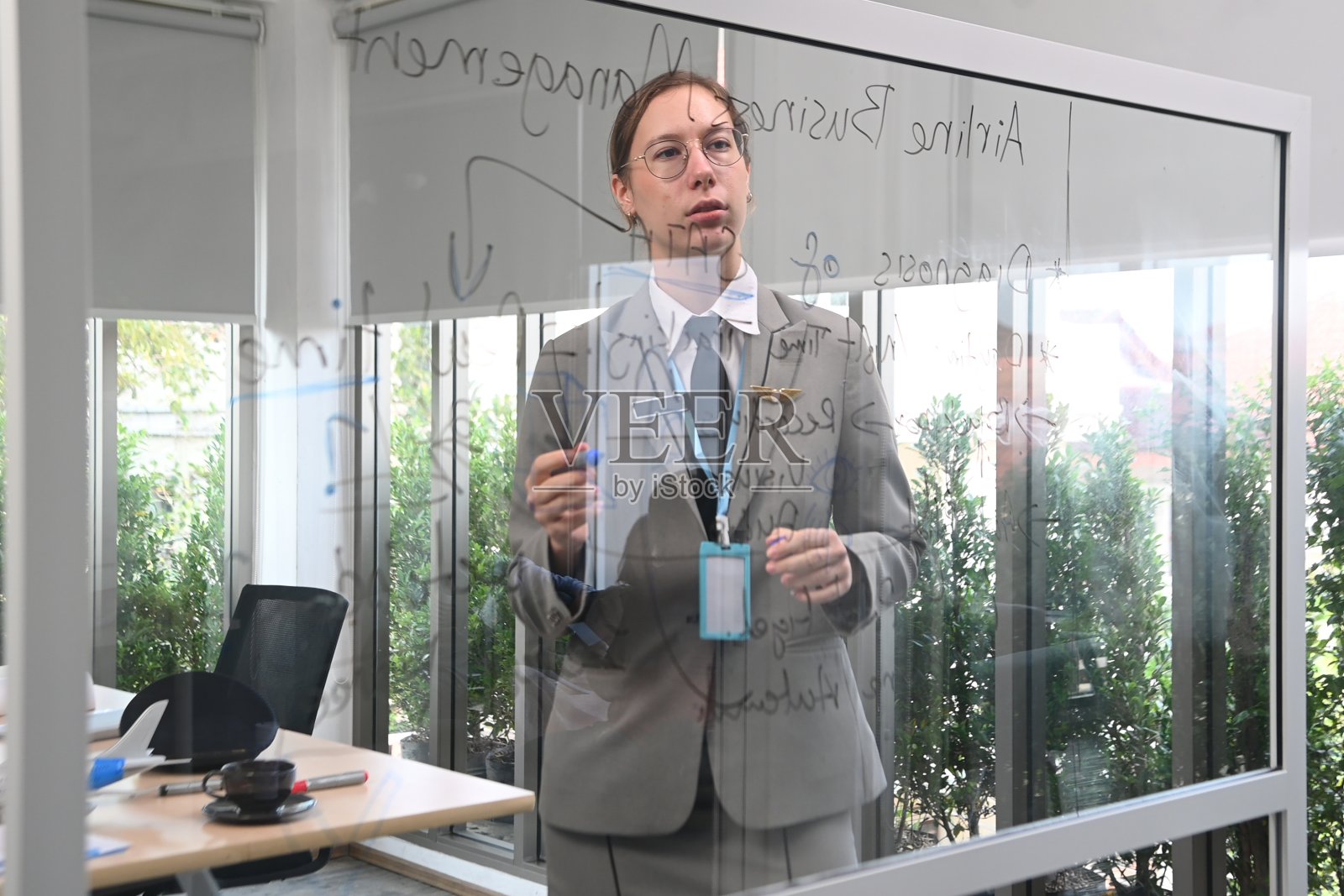 穿着飞行服的女人站在黑板前向同事们解释如何工作。照片摄影图片