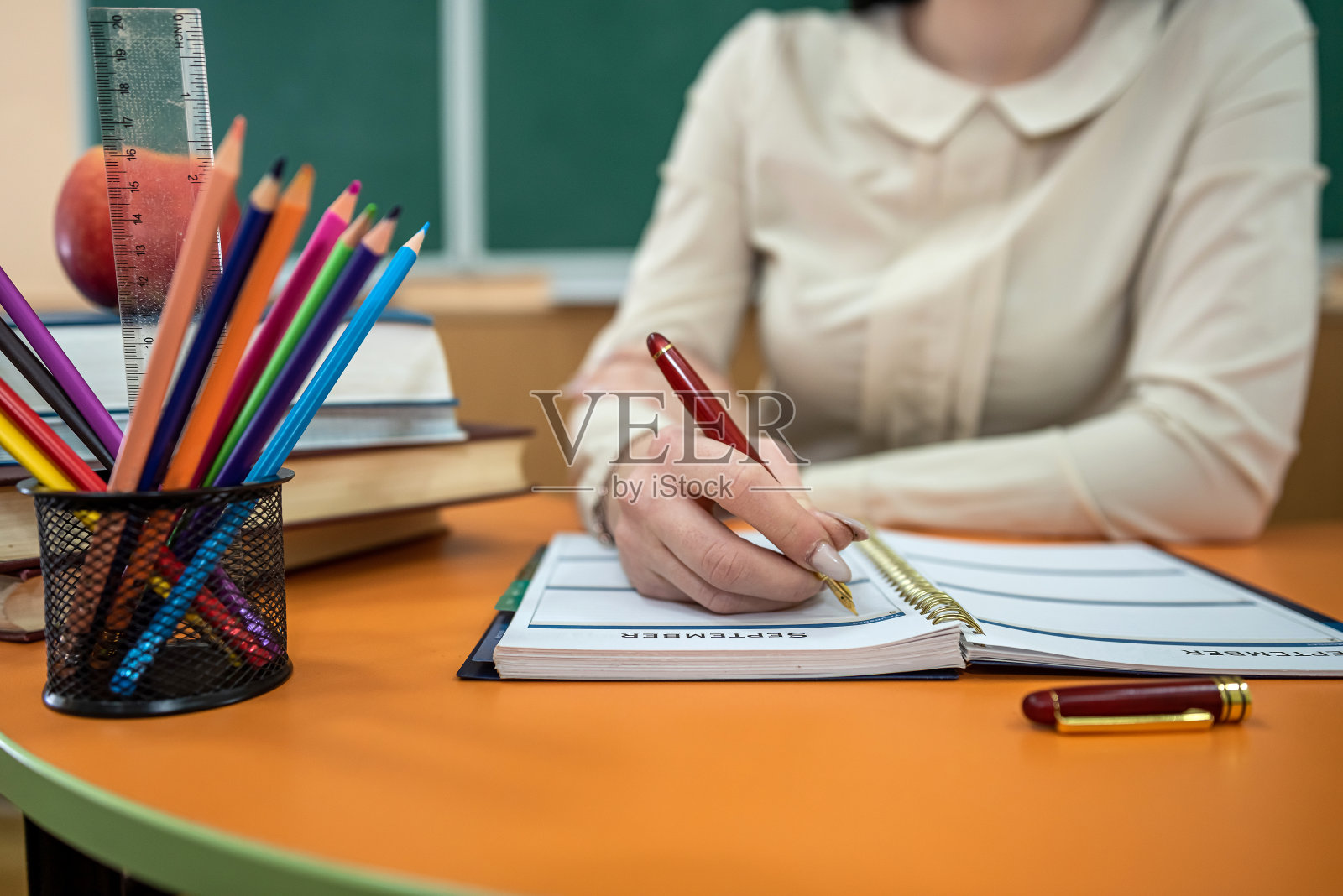 女教师坐在一张放着书和笔记本的桌子旁照片摄影图片