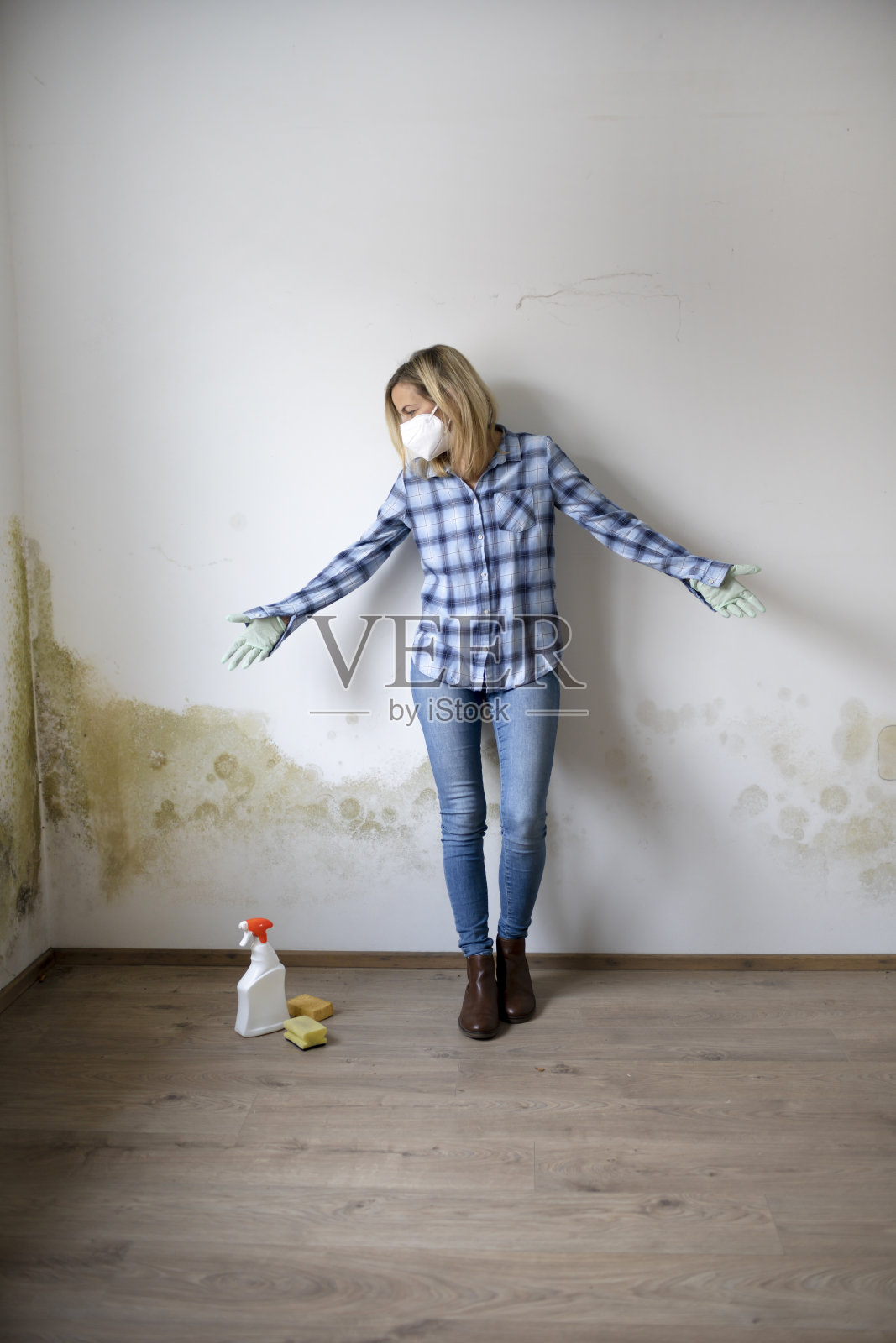 一个金发的年轻女子站在一堵长满霉菌的白色公寓墙前,沮丧而绝望照片摄影图片