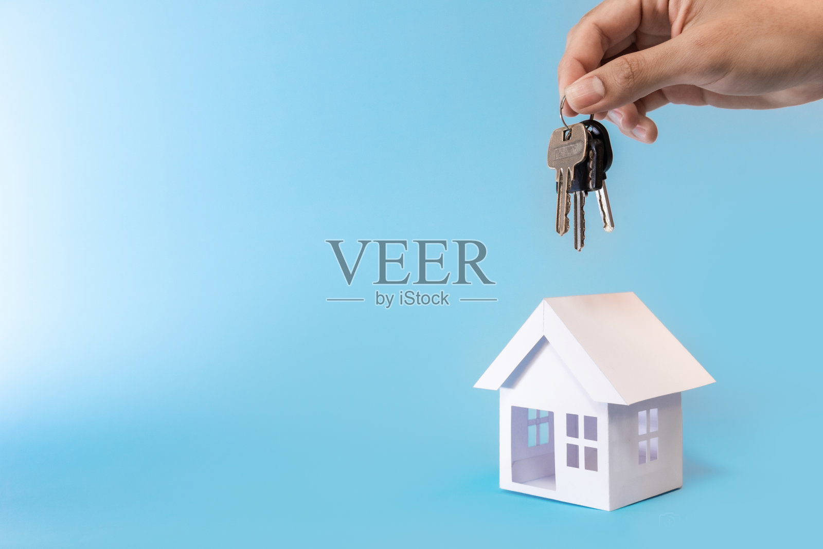 手握钥匙和白色房子模型在蓝色背景的再融资计划和房地产概念。照片摄影图片