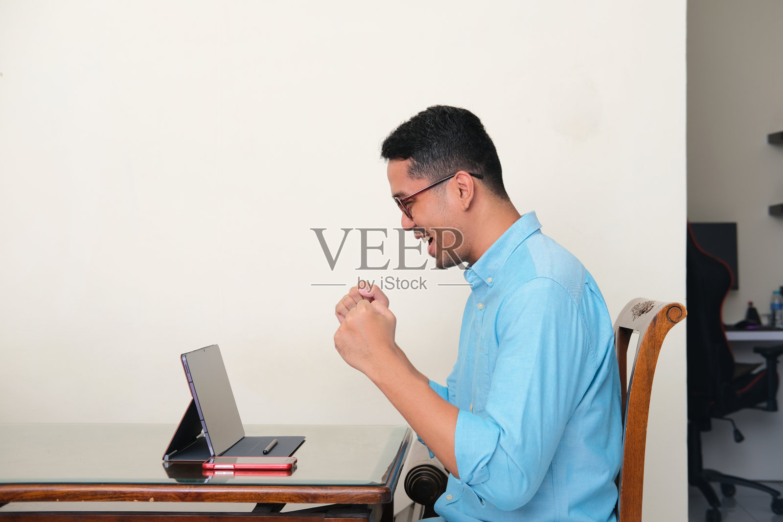 亚洲成年男子握紧拳头,看着自己的手机平板电脑屏幕,做出了成功的手势照片摄影图片