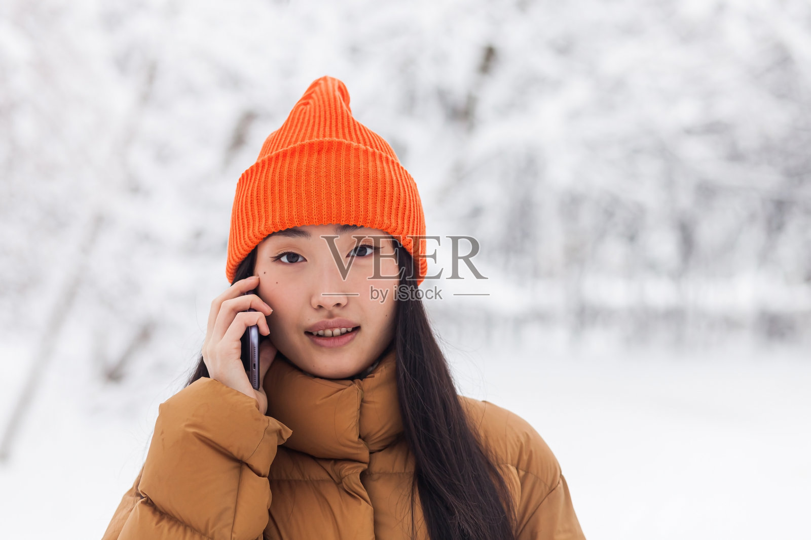 美丽的亚洲妇女在温暖的衣服,在一个冬天的雪天在公园的电话上散步照片摄影图片
