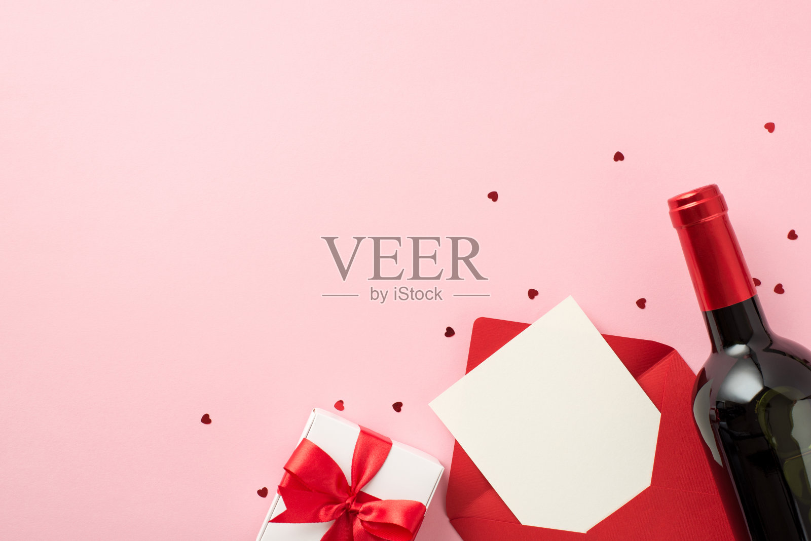 俯视图照片的情人节装饰心形纸屑白色礼盒与红色蝴蝶结红色信封纸和酒瓶在孤立的粉彩背景与空空间照片摄影图片
