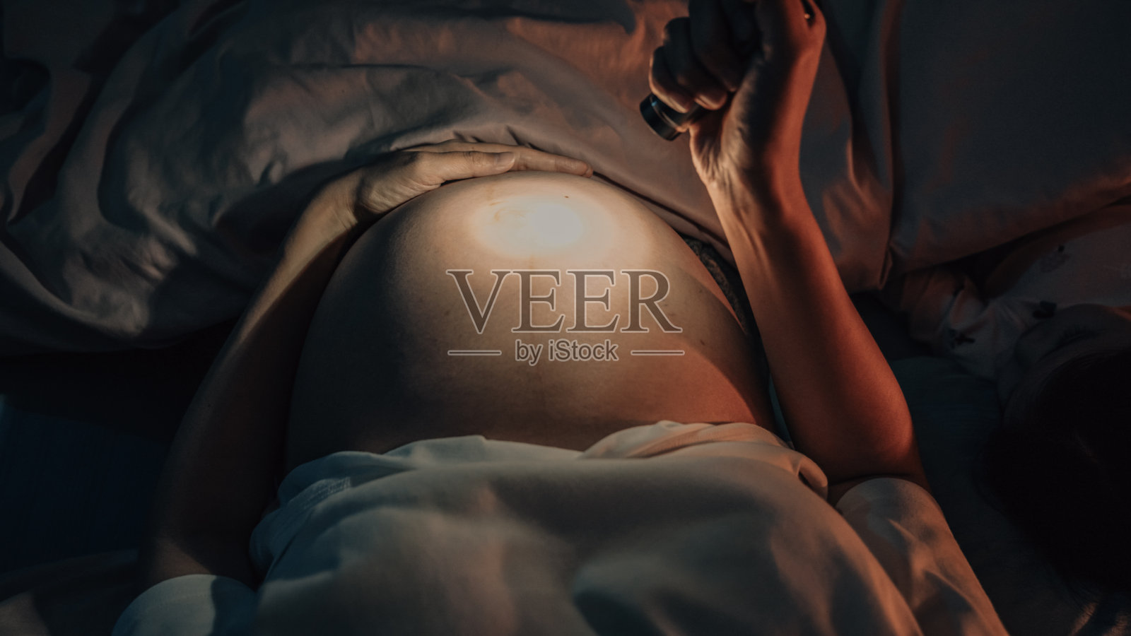 怀孕的女性在晚上很少睡觉的时候用手电筒或火炬照子宫。照片摄影图片