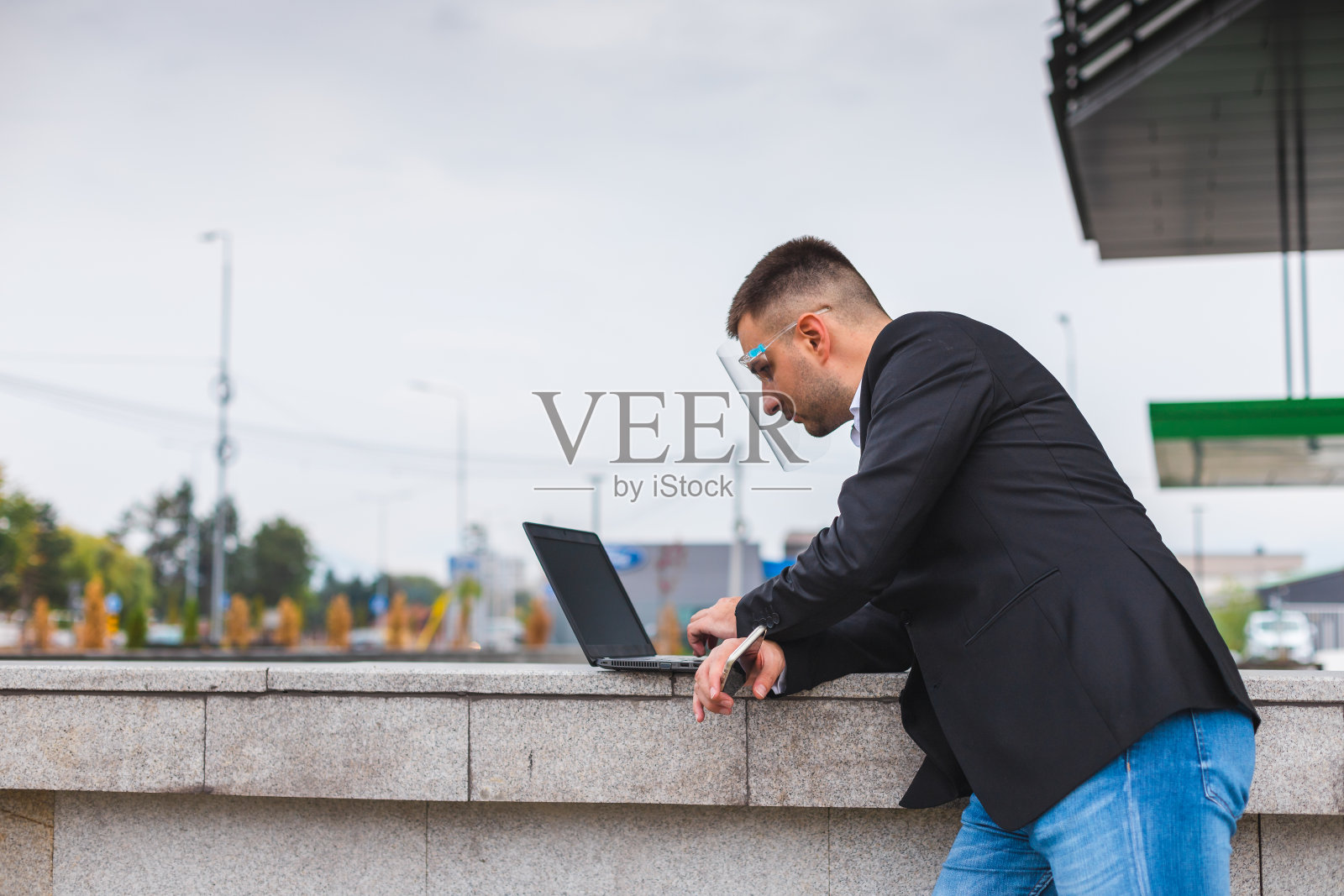 年轻英俊的白人商人穿着黑色西装,戴着面罩,在外面的城市场景中使用笔记本电脑照片摄影图片