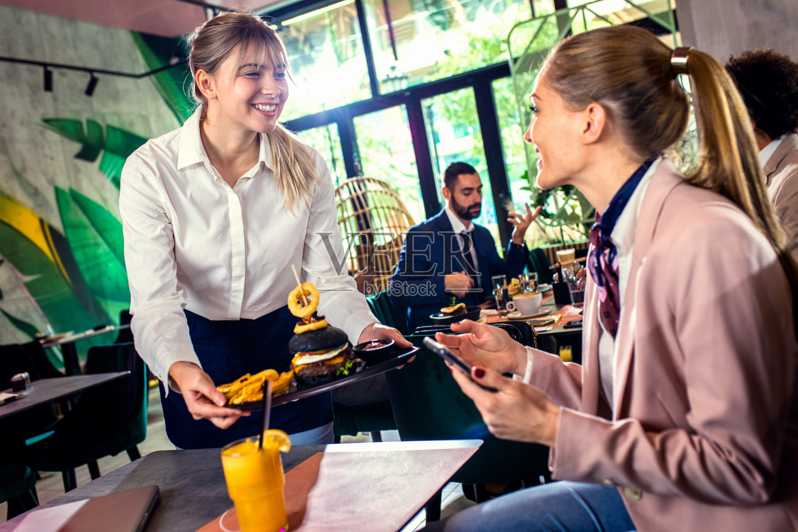 微笑的女服务员在餐厅为女商人服务。照片摄影图片