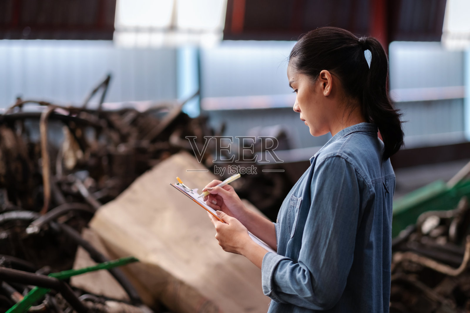 亚洲女工站在汽车发动机零件与复印空间的工厂。在车库里拿着剪贴板,检查旧发动机的库存清单。工业和股票概念。照片摄影图片