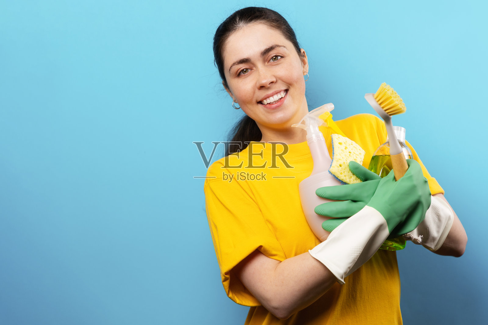一个面带微笑的白人年轻女子,戴着橡胶手套,手里拿着家用清洁产品。副本的空间。环保清洁理念照片摄影图片