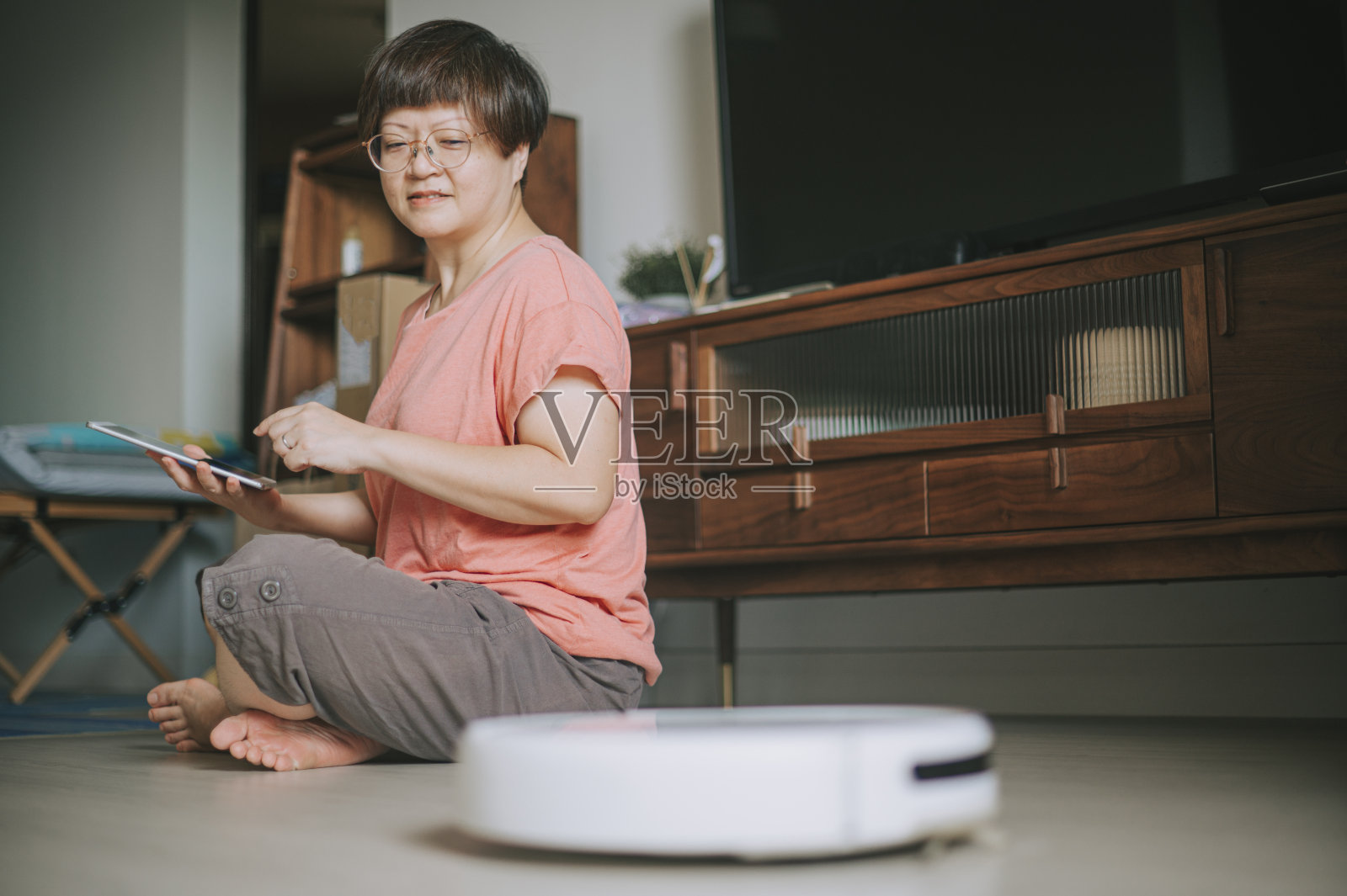 亚洲华人妇女在客厅用数码平板电脑控制机器人吸尘器照片摄影图片