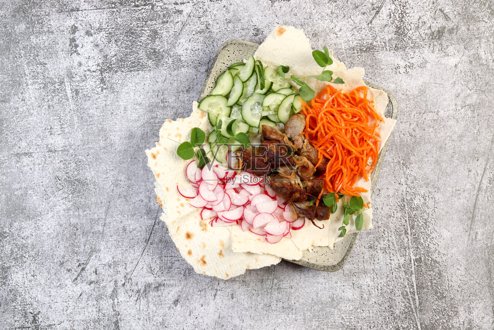 红烧猪肉与萝卜,黄瓜和胡萝卜在一个黑色背景的方形盘子。俯视图,平躺照片摄影图片