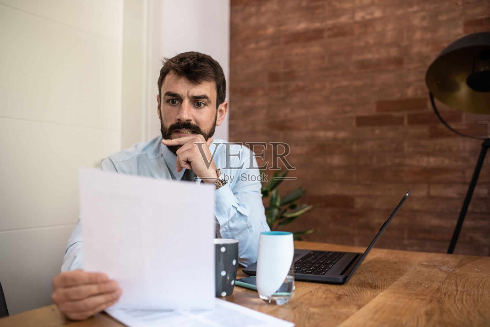 一个留着胡子的年轻人坐在这间办公室里,手里拿着一张纸。他在看文件,准备好了。照片摄影图片