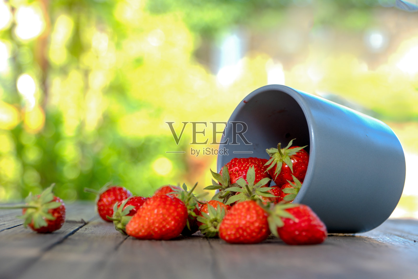 多汁的红草莓散落在花园里的一张木桌上。照片摄影图片