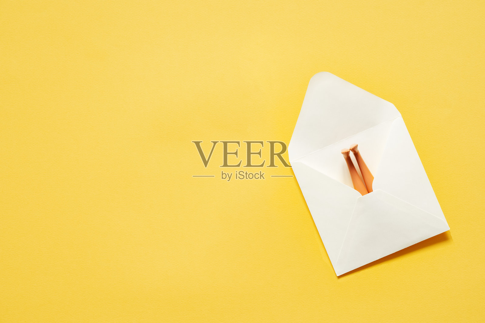 白色的纸信封,黄色的背景上,娃娃的腿伸出来照片摄影图片