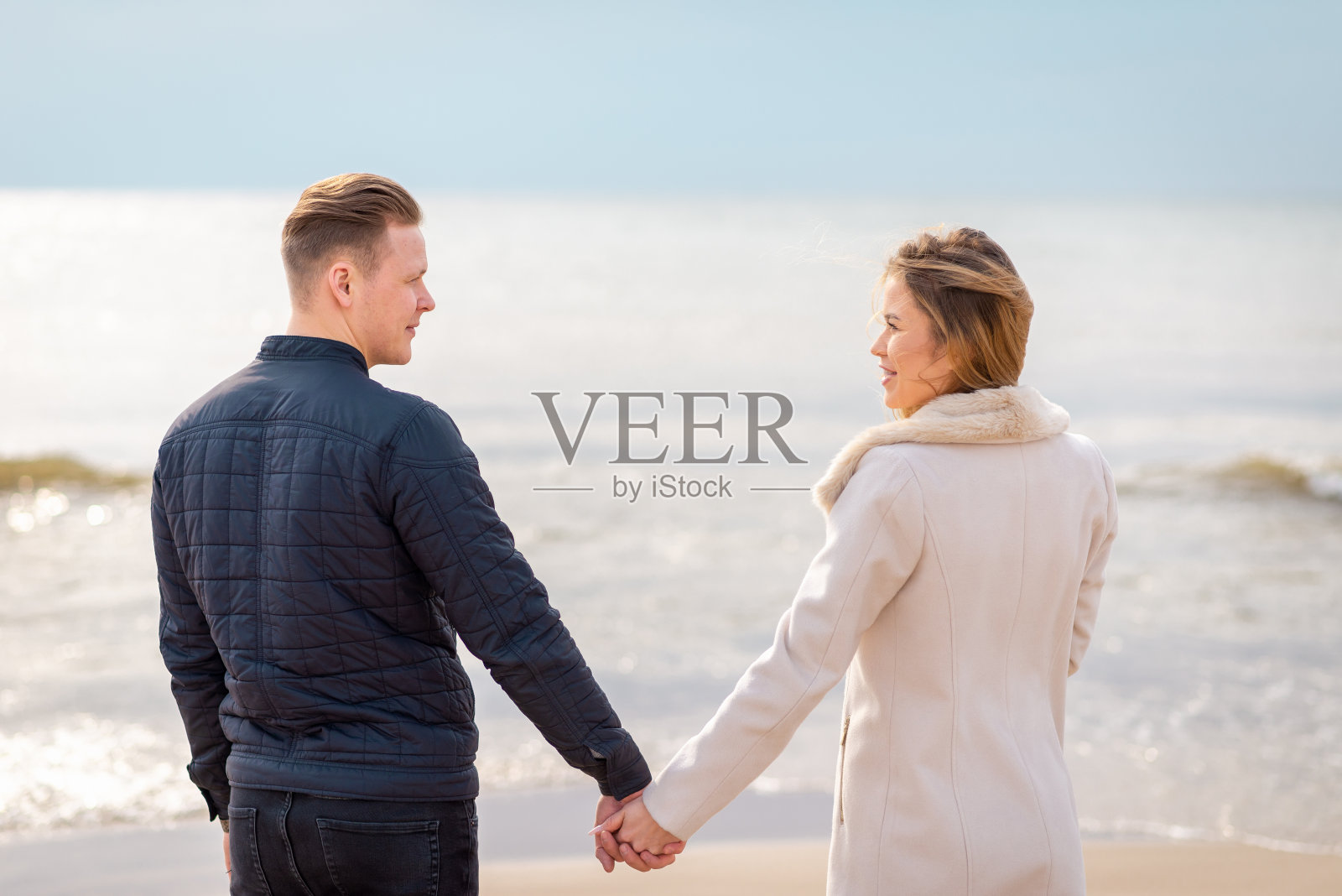 沙滩上的一对手牵着手夕阳西下。浪漫的年轻夫妇享受阳光,阳光,夫妇在春假。照片摄影图片