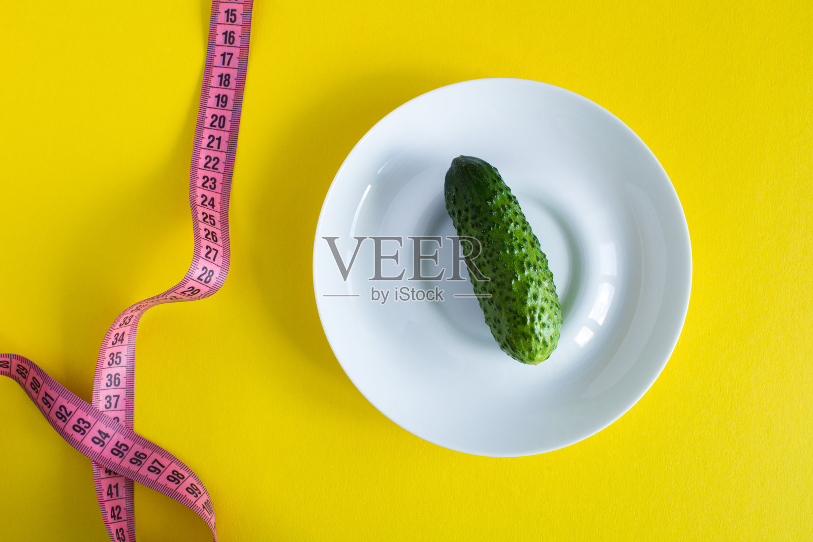 生黄瓜在白色的盘子和粉红色厘米黄色的背景。前视图。照片摄影图片