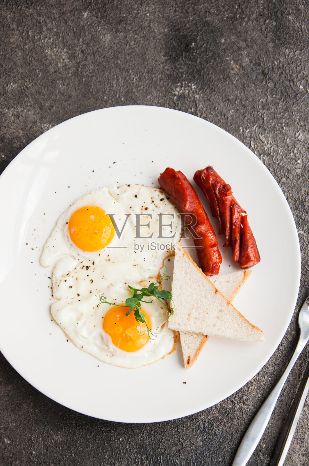 煎蛋和香肠放在灰色背景的白色盘子里。照片摄影图片