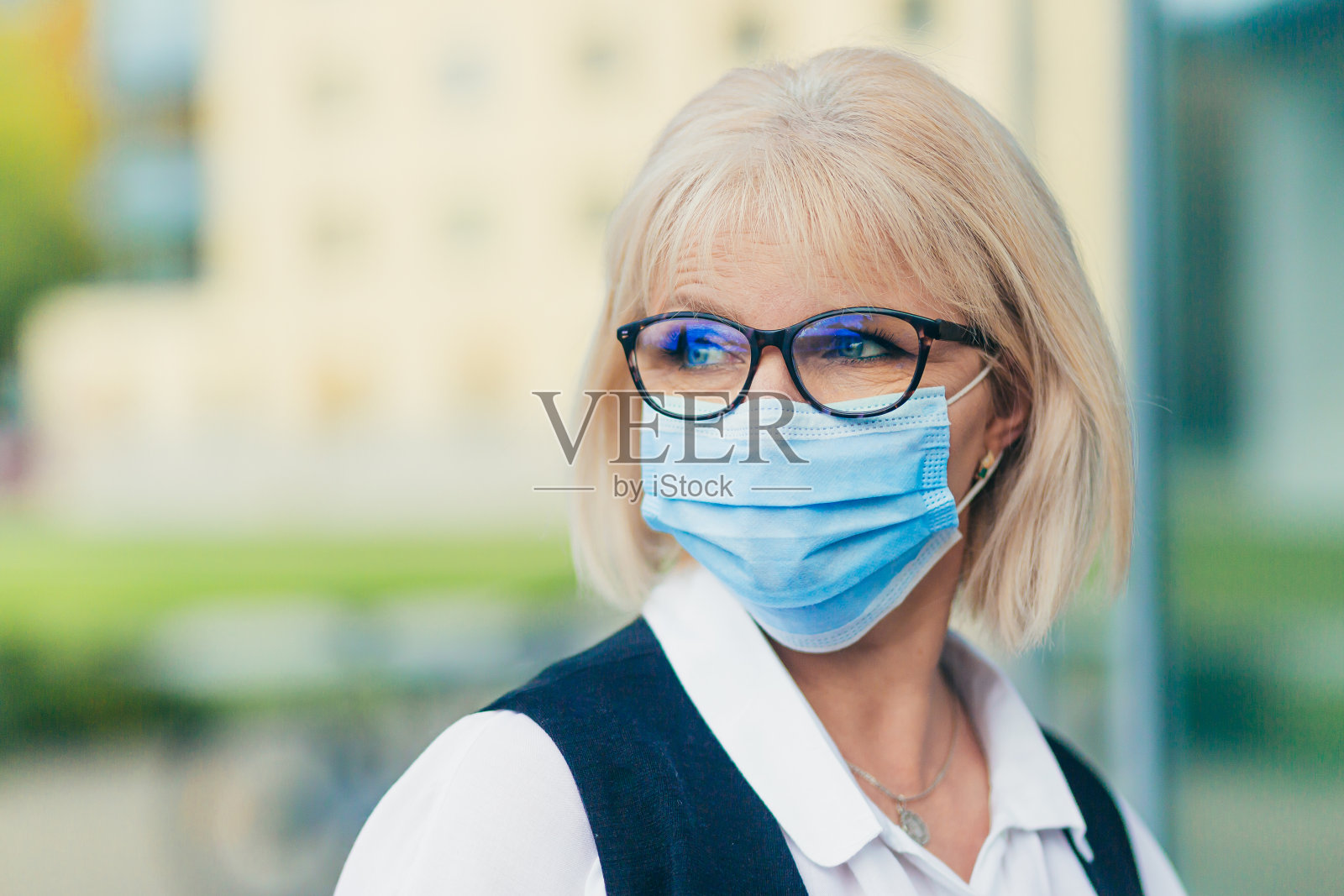 一个美丽的金发老年妇女的肖像,戴着蓝色医用口罩,戴着眼镜,户外,近距离,看着相机照片摄影图片