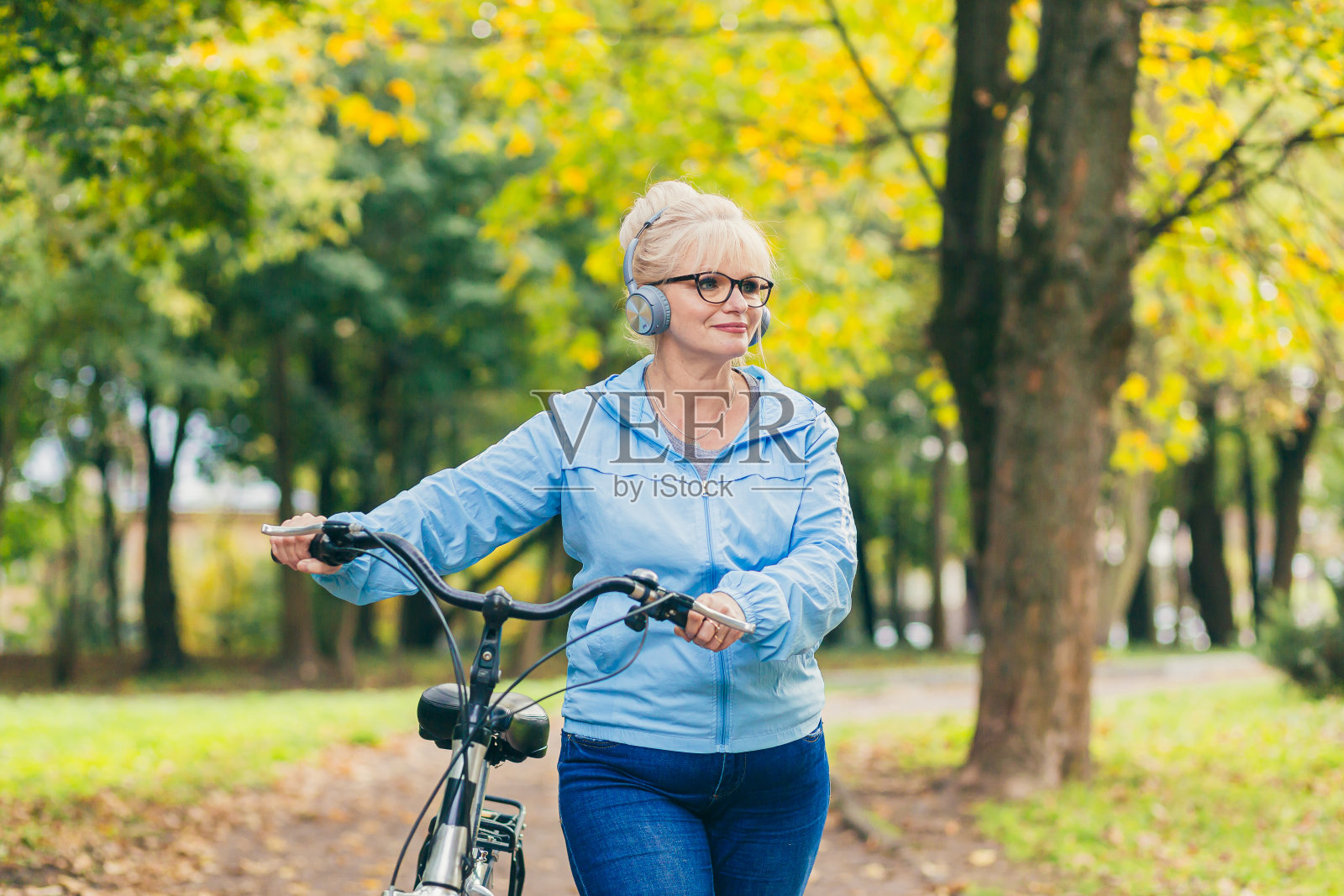 漂亮的金发女子在公园里骑自行车,在树林里,在大自然中,听音乐,花时间积极,玩运动,快乐照片摄影图片